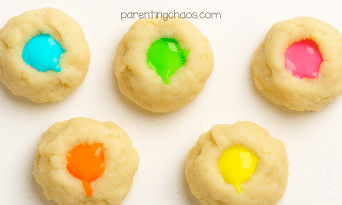 Five small balls of warm playdough with neon-colored glow paint puddled in the center of each, ready for mixing.
