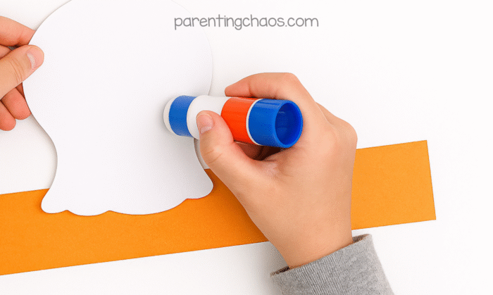 child gluing the cut out turkey head on to the orange paper head band