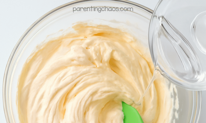 Contact solution being poured into a bowl of orange fluffy pumpkin pie slime mixture to activate the slime.