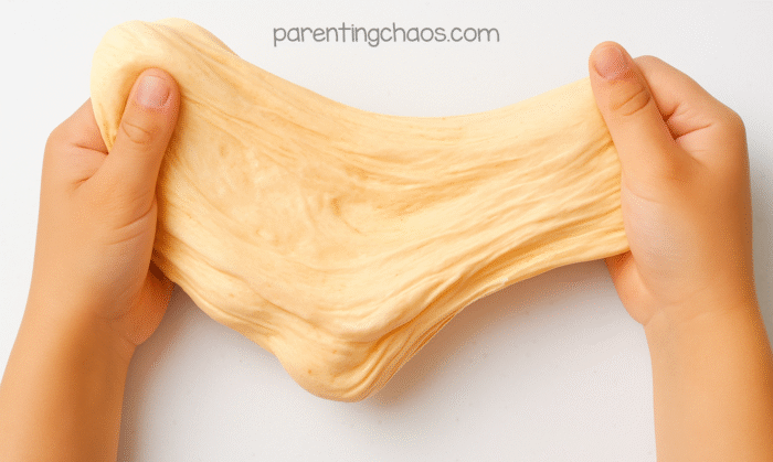 Child’s hands stretching fluffy pumpkin pie slime to show its smooth, stretchy texture.
