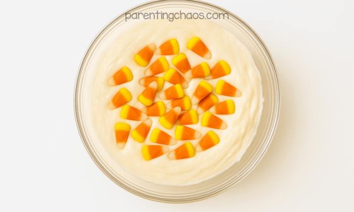 Melted marshmallow mixture topped with candy corn pieces before stirring, showing the start of the candy corn slime recipe.
