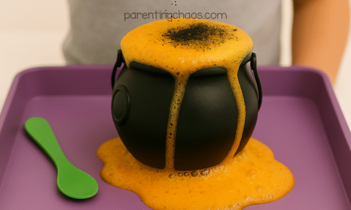 Black glitter is sprinkled over a fizzing orange potion inside a bubbling cauldron as part of a witches brew science activity.