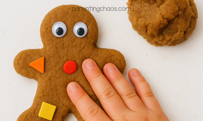 Close-up of child’s hand decorating a gingerbread man made from playdough with googly eyes and foam shapes.