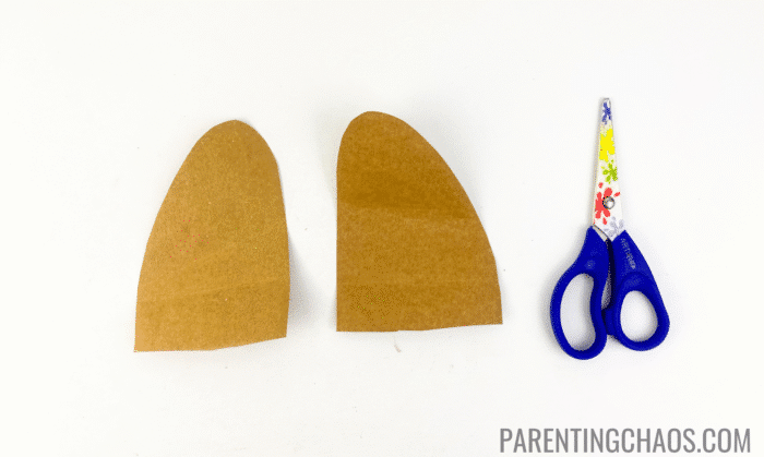 Two brown construction paper dog ears cut out next to a pair of child-safe scissors, shown as part of a paper plate dog craft activity.