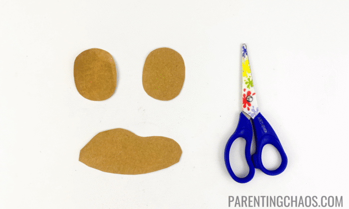 Brown construction paper cutouts for dog spots and eye patches next to a pair of child-safe scissors, ready for use in a dog paper plate craft.