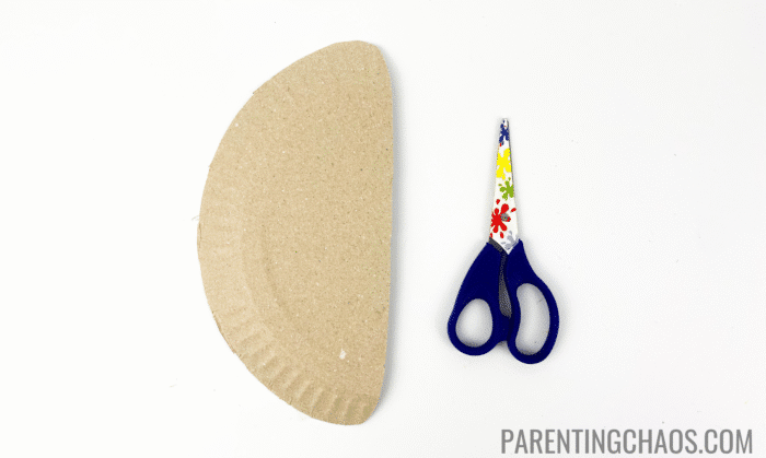Half-cut paper plate and kid-safe scissors with colorful flower designs, ready for a duck paper plate craft.