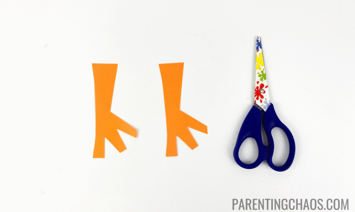 Two orange paper duck feet cut from construction paper next to colorful kid-safe scissors, ready for a duck paper plate craft