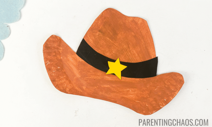 Paper plate cowboy hat craft painted brown with a black band and a yellow sheriff star in the center.