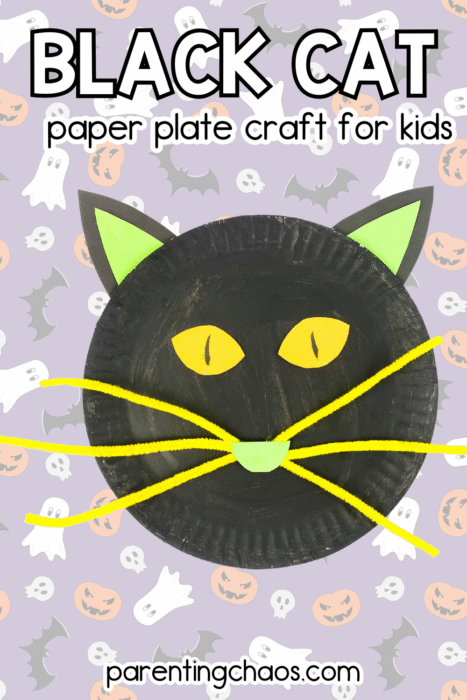 Black cat paper plate craft with green ears, yellow eyes, and bright yellow pipe cleaner whiskers on a purple Halloween background with ghosts, pumpkins, and bats.