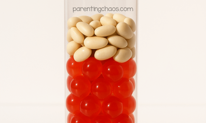 Layer of red water beads topped with fake navy beans inside clear sensory bottle.
