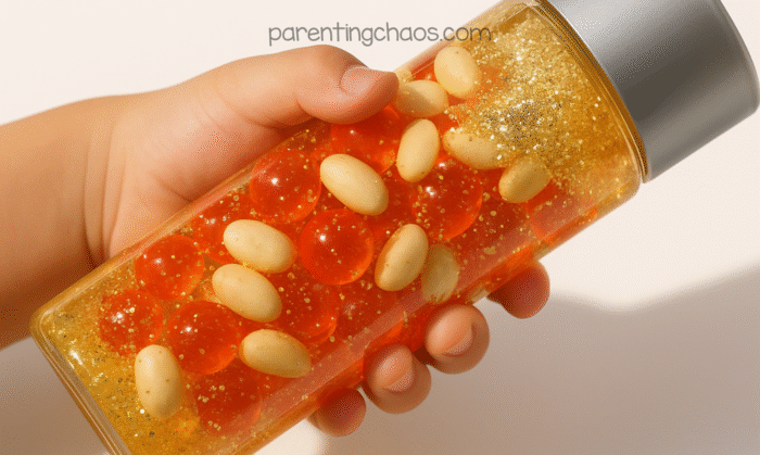 Child holding blood sensory bottle filled with red water beads, fake navy beans, and gold glitter