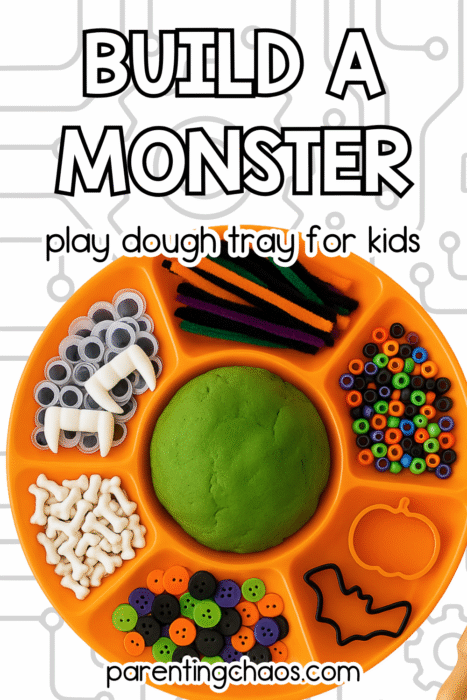 Overhead view of a bright orange playdough tray with Halloween loose parts including googly eyes, vampire fangs, buttons, bones, pipe cleaners, and beads.