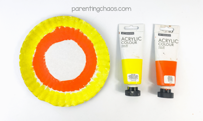 Paper plate painted in candy corn colors using orange and yellow acrylic paint for Halloween craft.