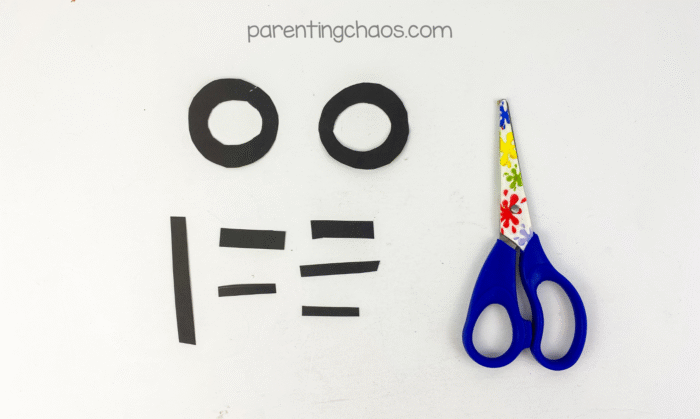 Black paper cut into small shapes for Frankenstein’s eyes and stitches, with scissors beside the pieces.