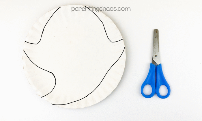 Paper plate with ghost shape outline drawn and scissors ready to cut.