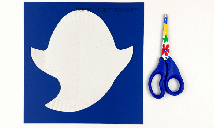 Cut-out paper plate ghost shape placed on dark blue paper.