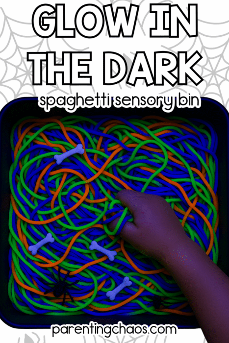 Child’s hand squishing neon green, blue, and orange glow-in-the-dark spaghetti with tiny plastic bones and spiders in a bin.