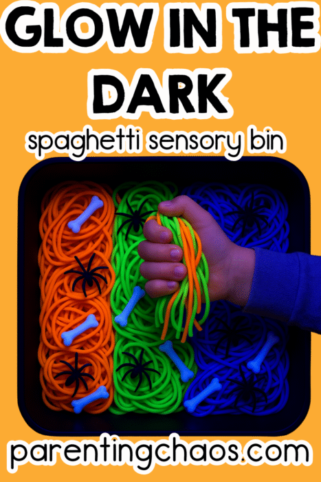 Hand holding a bundle of neon spaghetti over a sorted glow spaghetti bin with orange, green, and blue sections plus bones and spiders.