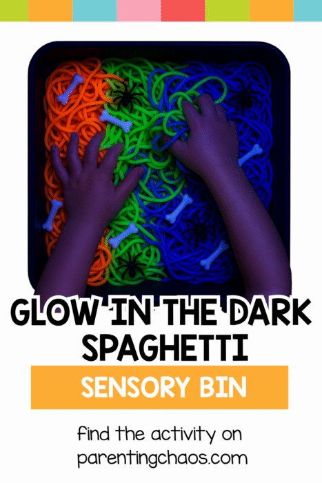 Two small hands exploring neon spaghetti under blacklight in a sensory bin with bones and spiders.