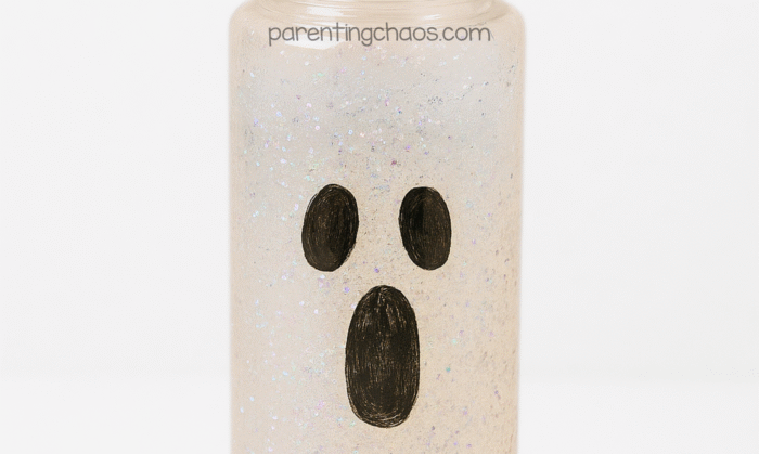 Close-up of ghost sensory bottle filled with glitter and clear liquid, showing black oval eyes and mouth design.