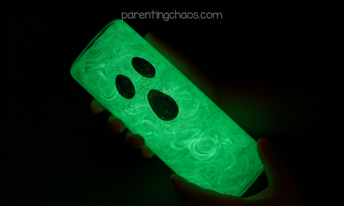 Child holding glowing ghost sensory bottle in the dark, with green light shining through the liquid.