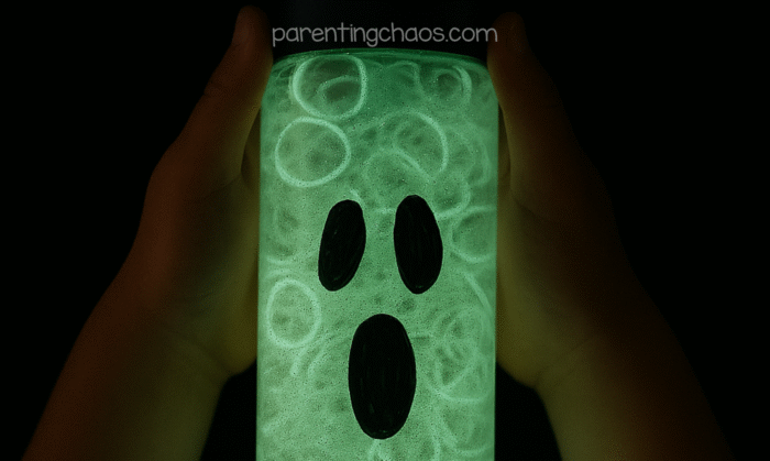 Hands holding glowing ghost sensory bottle in the dark, showing a bright green ghost face illuminated.