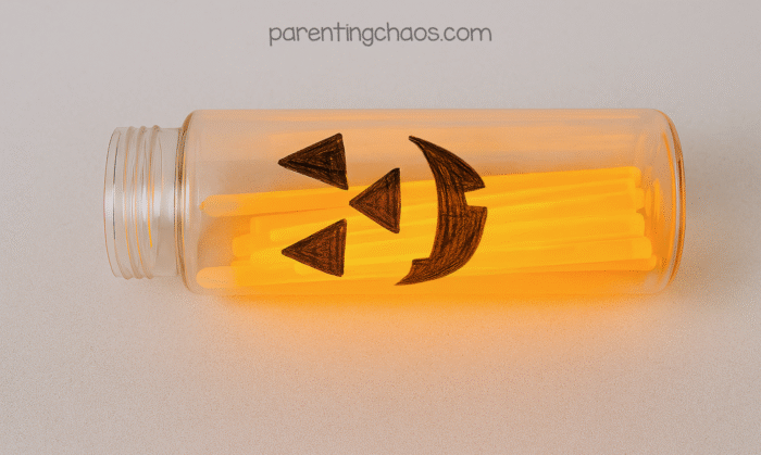 Clear bottle with a jack-o’-lantern face filled with orange glow sticks glowing from inside.