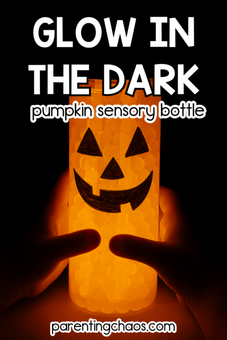 A child holds a glowing sensory bottle with orange water beads and a black jack-o’-lantern face drawn on the side. The bottle shines softly in the dark.