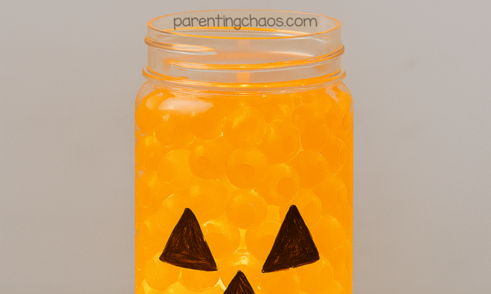 Close-up of a pumpkin sensory bottle filled with orange water beads glowing under light.