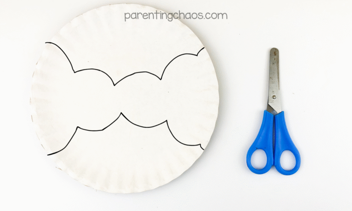 Paper plate with wing shapes traced in black marker next to blue scissors.