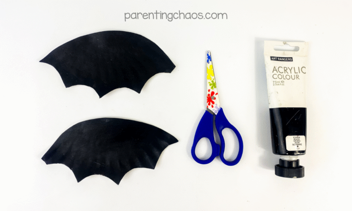 Two wing shapes cut out and painted black, scissors and black paint tube nearby.