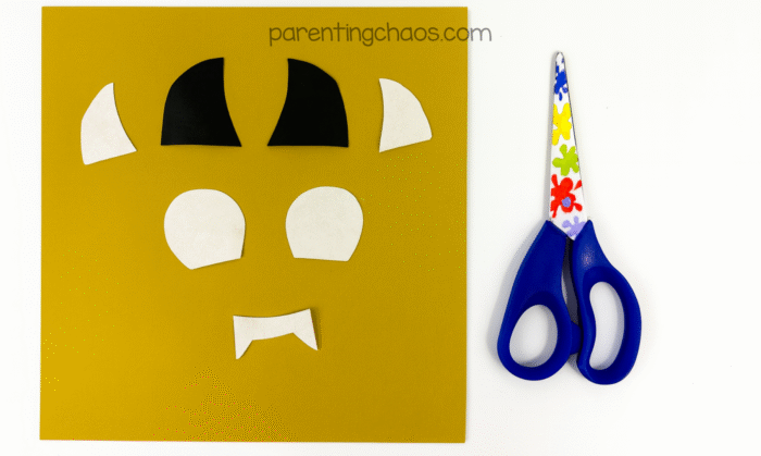 Black and white construction paper pieces for the bat’s facial features laid out on a gold background with scissors.