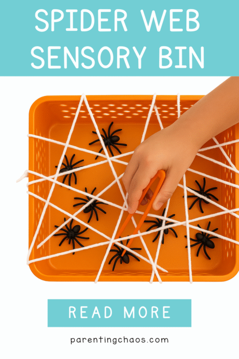 A child’s hand uses orange tweezers to grab a plastic spider from an orange sensory bin laced with white yarn “webs.” Text reads “Spider Web Sensory Bin – Read More.”