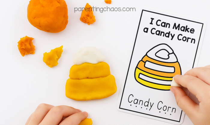 Child shaping orange, yellow, and white playdough into a candy corn beside an “I Can Make a Candy Corn” task card. The playdough candy corn matches the layered design on the card.