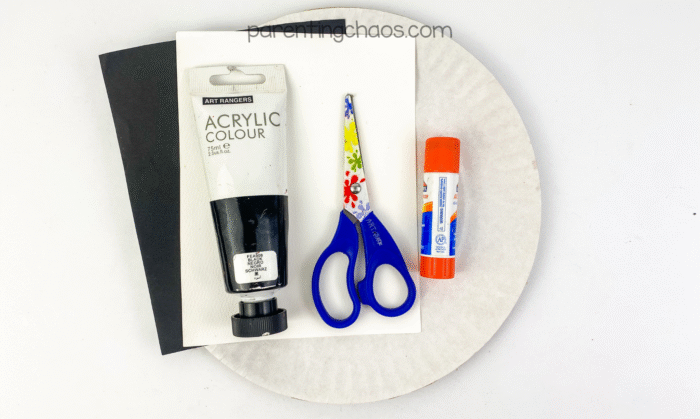 Paper plate, glue stick, preschool scissors, black acrylic paint, and construction paper laid out on a white background.