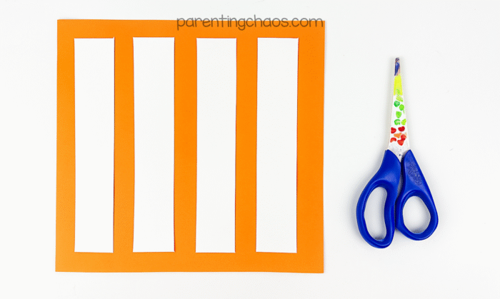 Orange construction paper with long strips cut out, scissors beside it.