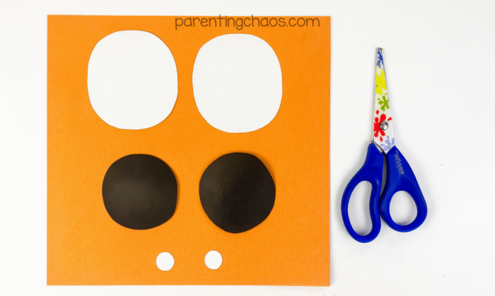 Black and white paper with large and small circles cut out for mummy eyes, scissors on the side.