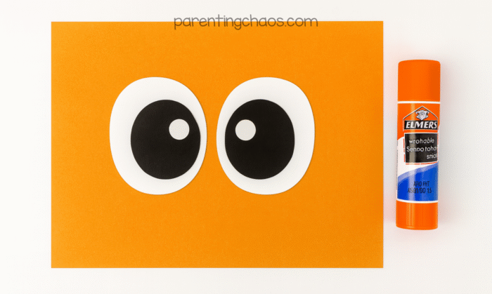 Two black and white paper eyeballs glued together on orange paper with a glue stick on the side.