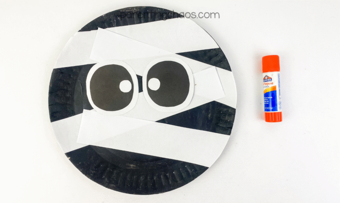 Paper plate mummy with strips and big cartoon eyes glued in the center, glue stick on the side.