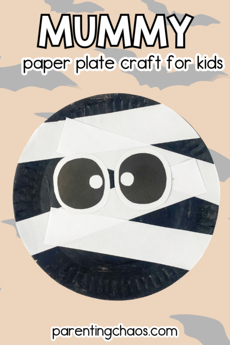 Halloween mummy paper plate craft with big cartoon eyes, wrapped in white paper strips on a black painted plate, set on a tan background with bats.