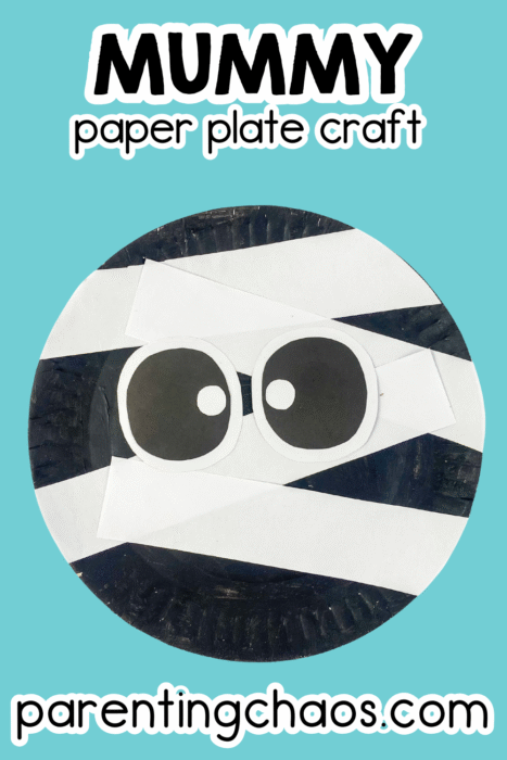 Close-up of mummy paper plate craft with large black-and-white eyes and white paper strips, on a blue background.