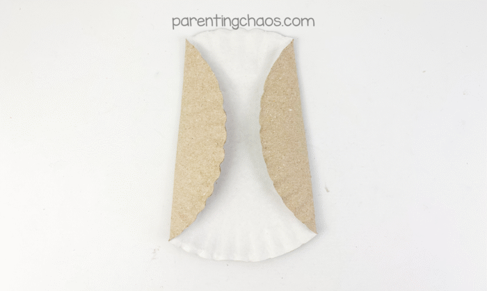 A paper plate folded inward on both sides with scalloped edges showing, creating the wings for an owl craft.