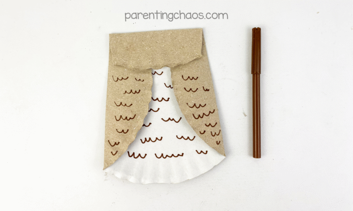 Brown marker drawing small feather-like squiggles on the paper plate owl wings and body to create texture.
