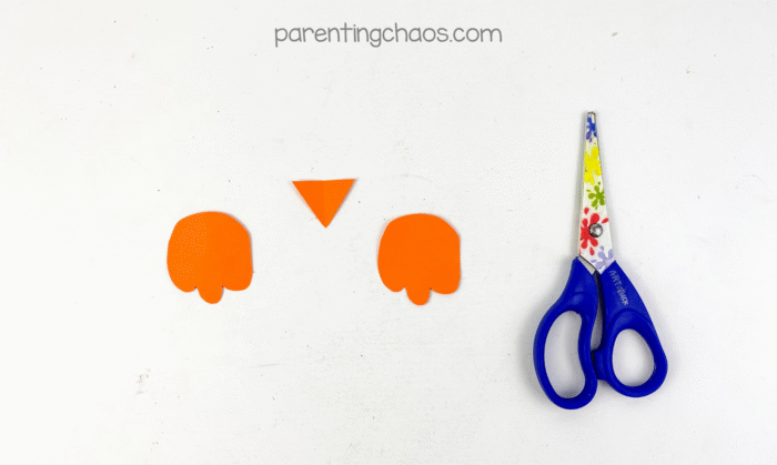 Two orange construction paper owl feet and a small orange triangle beak cut out with preschool scissors beside them.