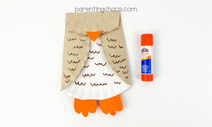 Orange feet and triangle beak glued to the owl paper plate body with an Elmer’s glue stick placed beside it.
