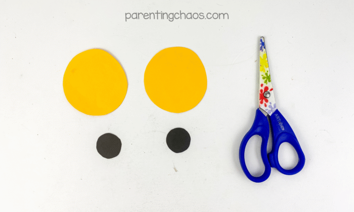 Two yellow circles and two smaller black circles cut from construction paper for the owl’s eyes, with preschool scissors next to them.