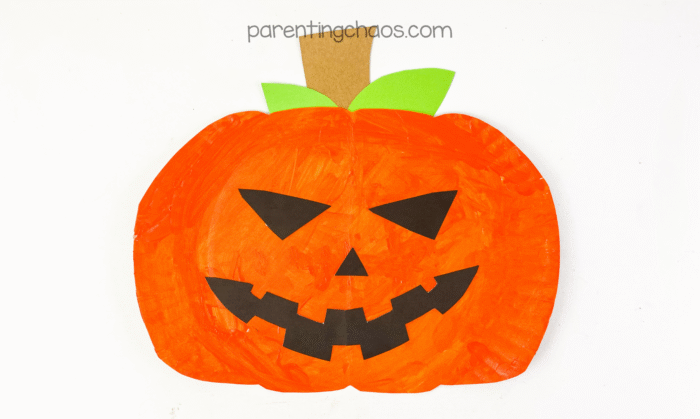 Finished paper plate Jack-o’-Lantern craft with orange paint, green leaves, and a big toothy smile, displayed on a white background.