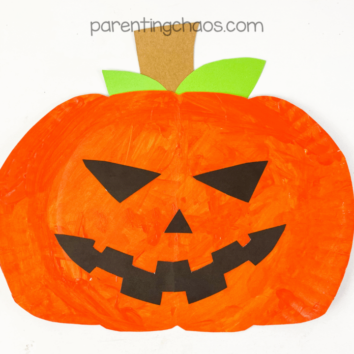 Finished paper plate Jack-o’-Lantern craft with orange paint, green leaves, and a big toothy smile, displayed on a white background.