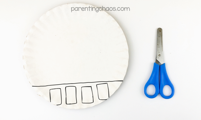 A white paper plate with a straight line and five rectangles drawn at the bottom, next to a pair of preschool scissors.