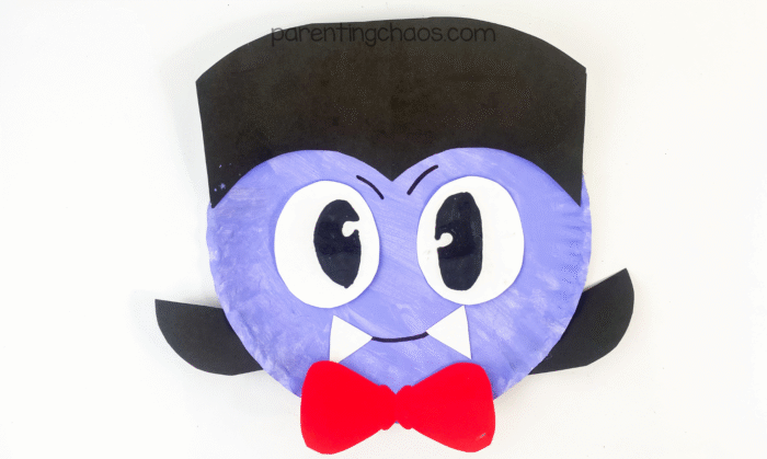 Completed vampire paper plate craft with black hair, big eyes, a red bow tie, and white fangs.